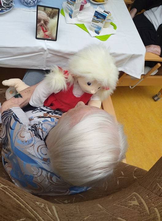Klientka hledící do zrcátka. V ruce drží terapeutickou panenku.